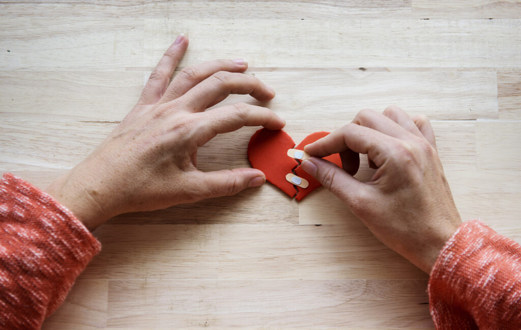 Hands bandaging a broken paper heart
