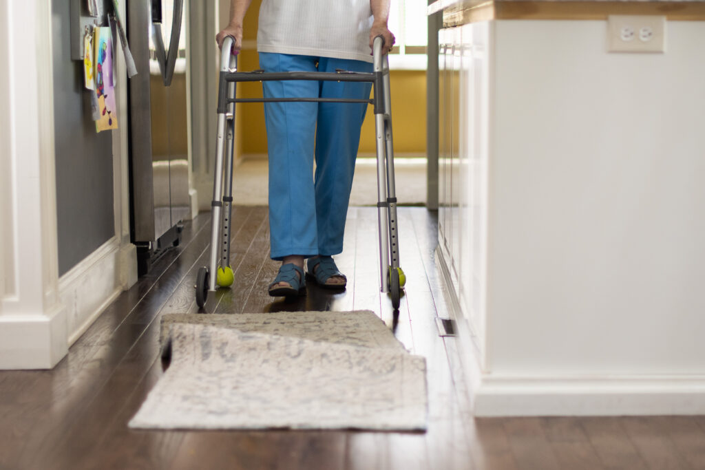 Person walking with walker approaches bunched rug.
